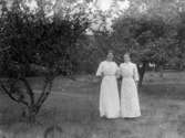 Gruppbild av två kvinnor fotograferade utomhus, i en trädgård med fruktträd.