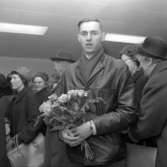 En man står i en folksamling med en bukett rosor i handen.