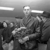 En man står i en folksamling med en bukett rosor i handen.