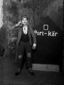 Revybild, utspökad man med texten ”port-kär” på hatten, ”vy 1920 A” på asken
	Metallutfällning.