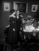 Ungt par i hemmiljö bredvid bord med blommor och presenter, lysning? 1919.