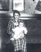 Fru Ester Alexandersson född 1893.08.16, död 1977.12.03 med sonen Egon, född 1933.07.07.
På väggen till höger hänger någon trycksak från Berlinolympiaden rubricerad 