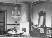 Rum med pappspända, blåmålade väggar samt upptill tryckt draperibård. Kolonnkakelugn. Inredning sannoligt från husets byggnadstid 1823.