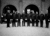 1934 Brandstationens jubileum, 9 men i uniformer framför brandstationen 
	Metallutfällning, repor, fläckar.