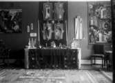 Ett Alta. bord, med dukat vävnad och bakom det finns tre vävnader med kyrkliga ikoner Löderups vävskola 1931
	Metallutfällning, fingeravtryck.