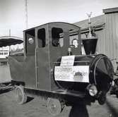 En cigarretrökande lokförare står redo att ge besökare på hantverksmässan i Kalmar 1947 en åktur med sitt motordrivna tåg.