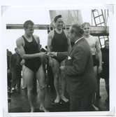 Från SM i simning, som 1946 hölls vid Långviksbadet i Kalmar.

 Nils Backlund medaljerar 2:an Rune Hellgren, Hellas. I mitten 1:an på 400 meter bröstsim John Rothman, SKK,till höger 3:an Bo Larsson, Västerås.