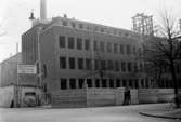 Gummifabrikens nya huvudkontor i sydöstra hörnet Joh Kocksgatan/Nygatan (idag 2016 Henry Dunkers gata) under uppförande hösten 1940. I bakgrunden skymtar Ångcentralen och fabriksskorstenen.