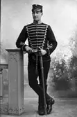 Porträtt ateljébild.  Bilden föreställer en miltär i helfigur. Sabel i vänster hand, höger hand vilar på ett staket. Bilden är ej ett originalfoto utan reproduktion av äldre bild. Beställare: Oscar Johansson. Thatstorp.