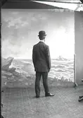 Mansporträtt, man stående i helfigur bakifrån iförd hatt. Ateljébild. Beställare: Sven Karlsson.