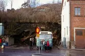 En samling människor står vid en blå buss på en busshållplats vid Gamla Torget i Mölndal, 1970-tal. Till höger ses del av huset Kvarnbygatan 41, tidigare brandstation och garage för polisbilar, numera Mölndals målarskola.

För mer information om bilden se under tilläggsinformation.