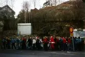 En samling ungdomar tågar förbi en busshållplats vid Gamla Torget i Mölndal, 1970-tal. Några av ungdomarna verkar ha glitter i håret och någon bär en tomtedräkt.

För mer information om bilden se under tilläggsinformation.