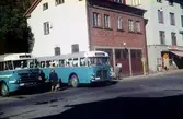 Två blå bussar står på en busshållplats vid Gamla Torget i Mölndal, 1950-60-tal. I mitten ses huset Kvarnbygatan 41, tidigare brandstation och garage för polisbilar, numera Mölndals målarskola. Till höger ses del av huset Kvarnbygatan 43, tidigare Mölndals stadshus, sedermera musikskola.

För mer information om bilden se under tilläggsinformation.