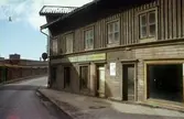 Kvarnbygatan vid Gamla Torget i Mölndal, ca 1962. På vänster sida av gatan ses Papyrus mur, på höger sid ses huset Kvarnbygatan 39, Nundstedts Speceriaffär. På fasaden sitter en affärsskylt med texten 