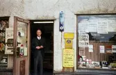 En man ståendes i dörren till tobakshandeln med adress Kvarnbygatan 43 vid Gamla Torget i Mölndal, 1960-tal.

För mer information om bilden se under tilläggsinformation.