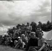 En gruppbild på barn som är framför ett tält i närheten av en sjöstuga.