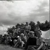 En gruppbild på barn som är framför ett tält i närheten av en sjöstuga.