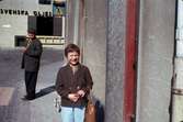 Lisbeth Sjöberg, dotter till Märta Sjöberg, fotograferad på trottoaren utanför Rasmussons skoaffär med adress Kvarnbygatan 4 vid Gamla Torget i Mölndal, ca 1961-1962. Längre bort på gatan står en man vid ett övergångsställe. I bakgrunden ses del av gaveln till huset Kvarnbygatan 6, byggnad tillhörande SOAB.

För mer information om bilden se under tilläggsinformation.