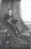 Helge Sandström med sitt dragspel fotograferad framför Emils ek på Ekudden.