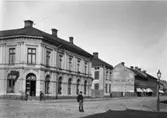 Drottninggatan österut från Järnvägsgatan ca år 1900. Hörnhuset uppfördes 1877, byggdes på med 2 våningar 1904 och ytterligare en 1955 till dagens utseende.