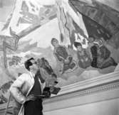 Konstnären Simon Sörman inspekterar sitt arbete med den nya utsmyckningen av Herrhagsskolans aula år 1949.