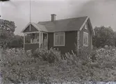 En stuga, två kvinnor och ett barn i Kalmar södra koloniområde, fotograferat omkring 1930. Kalmar södra koloniförening grundades 1917 och har idag 105 kolonilotter. Området ligger strax söder om länssjukhuset i Kalmar med huvudingång från Stensbergsvägen.
