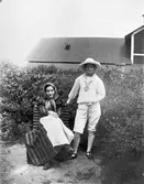 En person i randig klänning och schalett och Astrid Wilander i knälånga byxor. Möjligen är de utklädda.