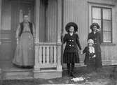 Kvinna på förstukvist vid okänt hus. Anna Sofia Wilander håller en liten flicka i handen. Systern Astrid Elisabet längst till höger.