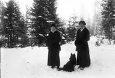 Två kvinnor och hund i vinterlandskap.