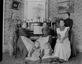 Gruppbild, kvinnor och barn vid piano.
