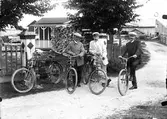Tre män med trampcyklar, motorcykel vid grinden.