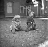 Två små barn sitter ute på gårdsplan
