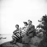 Två kvinnor och en man sitter på stenklippa vid vattnet
