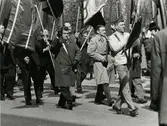 Första maj-tåg. Tage Drost, i mitten på bild med mörk överrock och mörka handskar.