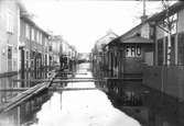 Vårfloden år 1916. Långgatan i Bollnäs mot sydväst. Bilden tagen ungefär från platsen för dåvarande apoteket. Till vänster syns Apelgrens affär, till höger Palmérs urmakeri.