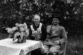 Storvik-Hammarby. Man och kvinna sitter ute vid trädgårdsmöblerna omgiven av syrener. Den 8 juni 1950