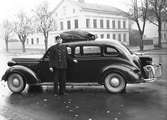 Chaufför P J Green vid en X307 förlängd 1937  Dodge D-5 Touring Sedan med gengasaggregat på Teaterplan vid Staketgatan i Gävle. I bakgrunden Norra Rådmansgatan 20. I bakgrunden Sjöströms mekaniska verkstad.