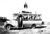 Nils Anderssons buss, Derome omkring 1927. Busslinjen Veddige - Varberg. En man står i dörröppningen i bussen, där passagerare sitter och på busstaket står en man vid bagaget.