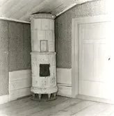 Stommen, huvudbyggnaden. Kakelspis på träfötter. Övervåningen. Kaklet övermålat med krita. På mitten har kakelspisen en liten nisch. Träfötterna och bottenplattan av trä har bevarats.