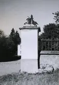 Portstolpar vid entren till mangården. Av kalksten, vitputsade. Ryttaren är utskuren i järnplåt och svartmålad.