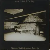 Interiör från Blekingestugan, även kallad Kyrkhultsstugan, på Skansen. På bilden syns målade och vävda bonader på väggarna, ett dukat bord, spinnrock, golvur m.m.