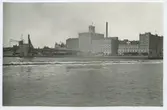 Byggnaderna vid kvarteret i mitten-höger är Ångkvarnen och byggnaderna vid kvarteret till höger är Riskvarnen från 1937.
