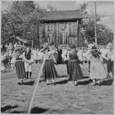 Män och kvinnor i folkdräkt som dansar, utomhus.