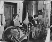 Två kvinnor vid varsin spinnrock.