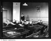 I Åmots småskola. Lärarinnan Elna Lindberg med skolbarn, från vänster: Anders Norgren, John Åberg, Nanny Brodin (gift Byström), Göta Waller, Agnes Pettersson, Sigvard Sundgren, Gösta Jonsson, ej namngiven person, Anny Groth, Ture Larsson, Svea Karlsson samt Nanny Larsson (West).