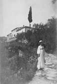 Ester Ellqvist-Bauer i Italien. Hon står på en stenlagd väg upp mot ett bostadshus.