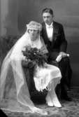 Bröllopsbild på en kvinna i brudklänning hållandes i en blombukett. Mannen har frack. Enligt Walter Olsons journal är bilden beställd av herr Axel Karlsson.