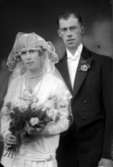 Bröllopsbild. En kvinna i brudklänning hållandes i en blombukett och en man i kostym. Enligt Walter Olsons journal är bilden beställd av magister H Lindström.