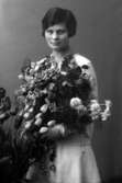 Ateljébild på en kvinna med en blombukett. Enligt Walter Olsons journal är bilden beställd av bonde fr Vivi.