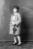 Ateljébild på en flicka med kappa och mössa. Enligt Walter Olsons journal är bilden beställd av Mary Holmquist.
